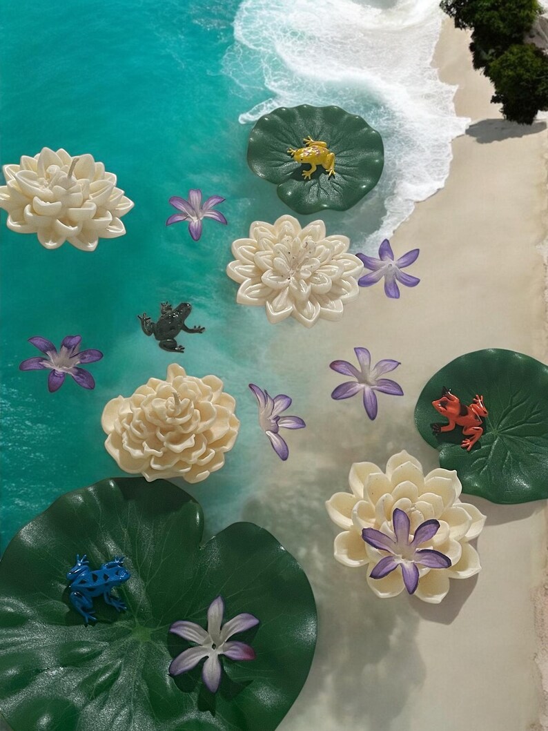 May include: A white and green resin art piece with a beach scene. The scene includes white sand, blue water, and green lily pads with frogs and flowers.