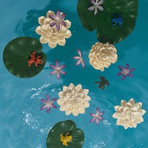 May include: A blue background with white water lily flowers and green lily pads. There are also small frogs in various colors on the lily pads.
