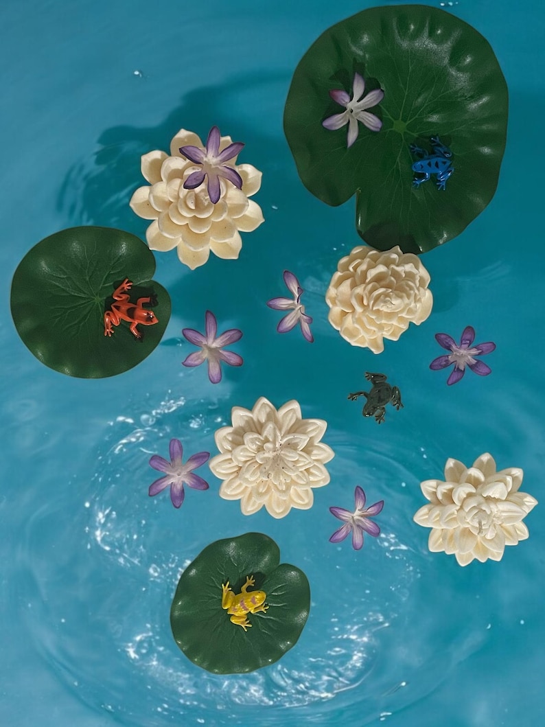 May include: A blue background with white water lily flowers and green lily pads. There are also small frogs in various colors on the lily pads.