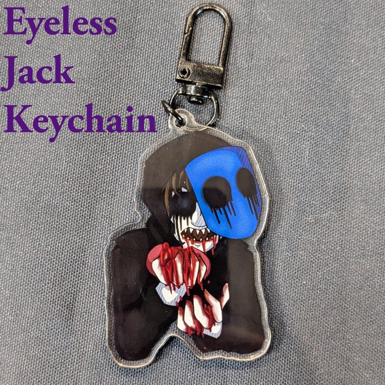 May include: A clear acrylic keychain featuring a character with a blue mask, black hoodie, and holding a bloody heart. The keychain has a silver clasp and the text "Eyeless Jack Keychain" in purple.