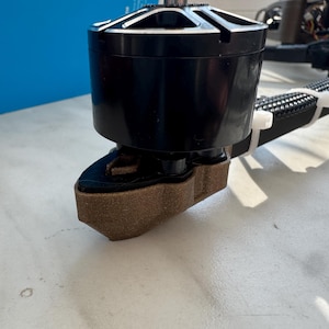 Puede incluir: Primer plano de un tren de aterrizaje de color marrón impreso en 3D para un dron. El tren de aterrizaje está unido a un motor negro.