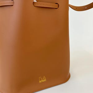 K&ouml;nnte beinhalten: Eine braune Ledereimer-Tasche mit einem goldenen Logo, auf dem "LA BAGUETTE" steht.