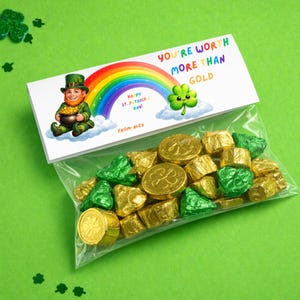 Op de afbeelding: Een doorzichtige cellofaan zak gevuld met goud en groen folie verpakte chocolade snoepjes. De zak is bedekt met een witte kaart met een regenboog, een kabouter en de tekst "YOU'RE WORTH MORE THAN GOLD". De kaart zegt ook "Happy St. Patrick's Day!" en "From Alex."