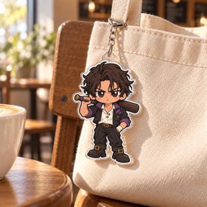 Puede incluir: Un llavero de acrílico con un personaje de dibujos animados de cabello oscuro y desordenado, que viste una chaqueta negra sobre una camisa blanca, pantalones oscuros y botas. El personaje sostiene un bate de béisbol sobre el hombro.