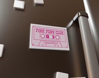 May include: A white cassette tape magnet with the text "PINK PONY CLUB" and "Chappell Roan" in pink lettering. The magnet is on a brown refrigerator.