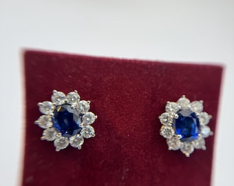 May include: A pair of silver stud earrings with a blue oval gemstone surrounded by smaller clear gemstones.