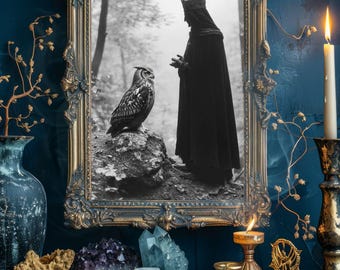 May include: A framed black and white image of a person in a crown and cloak with an owl. The ornate gold frame is surrounded by a dark blue wall. A lit candle, crystals, and tarot cards are on a wooden surface.