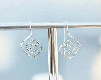 May include: A pair of silver earrings with a spiral design inside a square shape.