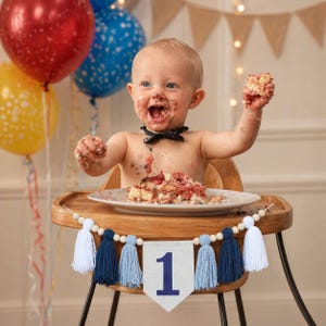May include: A baby covered in cake sits in a wooden high chair, celebrating a first birthday. The baby wears a black bow tie and holds a piece of cake. A banner with the number "1" and tassels decorates the high chair.