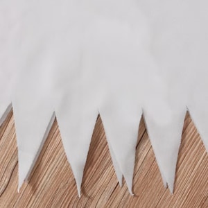 May include: A solid white fabric piece featuring a jagged, triangular hemline. The material has a smooth, opaque texture and is cut into a series of sharp, pointed sections along the bottom edge, creating a distinct sawtooth pattern throughout.