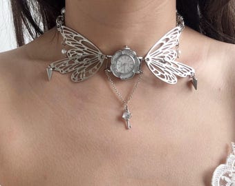 May include: Silver-toned choker necklace featuring butterfly wing designs and a small clock face at the center. A delicate chain suspends a key pendant. The necklace has a vintage, gothic aesthetic.