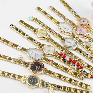 Puede incluir: Una colección de relojes de pulsera de tono dorado con varios encantos y diseños. Los relojes presentan diferentes estilos de esfera, incluyendo redonda, ovalada y rectangular. Algunos encantos incluyen cerezas, ojos malos y flores.
