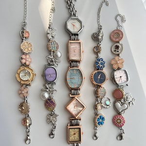May include: Several vintage wristwatches with decorative chains. The watches have square, rectangular, and octagonal faces, with floral and charm accents. The watch faces display different colours and designs. The chains are silver-toned.