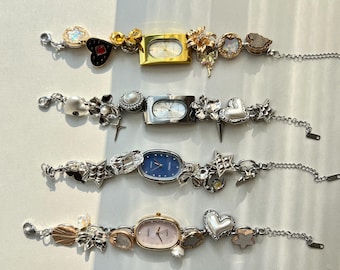 May include: Four silver and gold wristwatches with decorative charms. Each watch has a different colored face: white, blue, pink, and gold. The charms include hearts, stars, flowers, and other decorative elements.