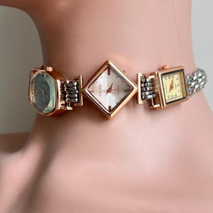 May include: A statement choker necklace with three watch faces in gold and silver. The watch faces are square, diamond, and rectangular, with silver and gold metal accents. The necklace is a unique piece of jewellery.