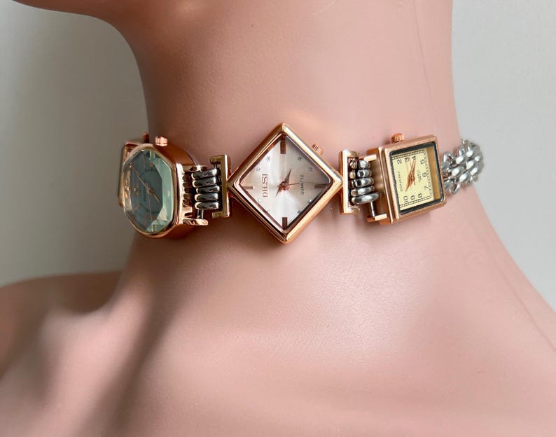 May include: A statement choker necklace with three watch faces in gold and silver. The watch faces are square, diamond, and rectangular, with silver and gold metal accents. The necklace is a unique piece of jewellery.