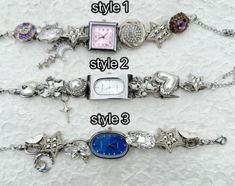 May include: Three silver charm bracelets with different watch faces. The first bracelet has a pink watch face with silver charms, including a star, a crescent moon, and a heart. The second bracelet has a white watch face with silver charms, including a heart, a star, and a cross. The third bracelet has a blue watch face with silver charms, including a star, a butterfly, and a heart.