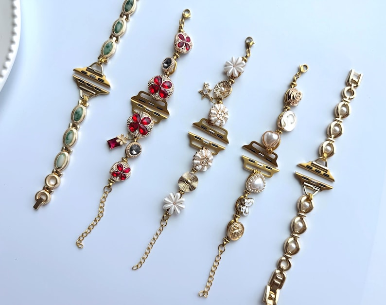 May include: Five gold-toned bracelets with various decorative elements. One bracelet features green oval stones, while others showcase red floral accents, white flowers, pearls, and other embellishments. Each bracelet has a unique design and a chain closure.