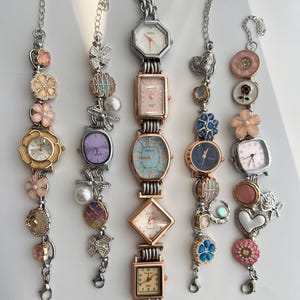 May include: Several decorative bracelet watches with diverse face shapes and embellishments. The watches have silver-tone chains and are decorated with floral, pearl, and gemstone accents. The watch faces come in a variety of colours, including white, pink, and blue.