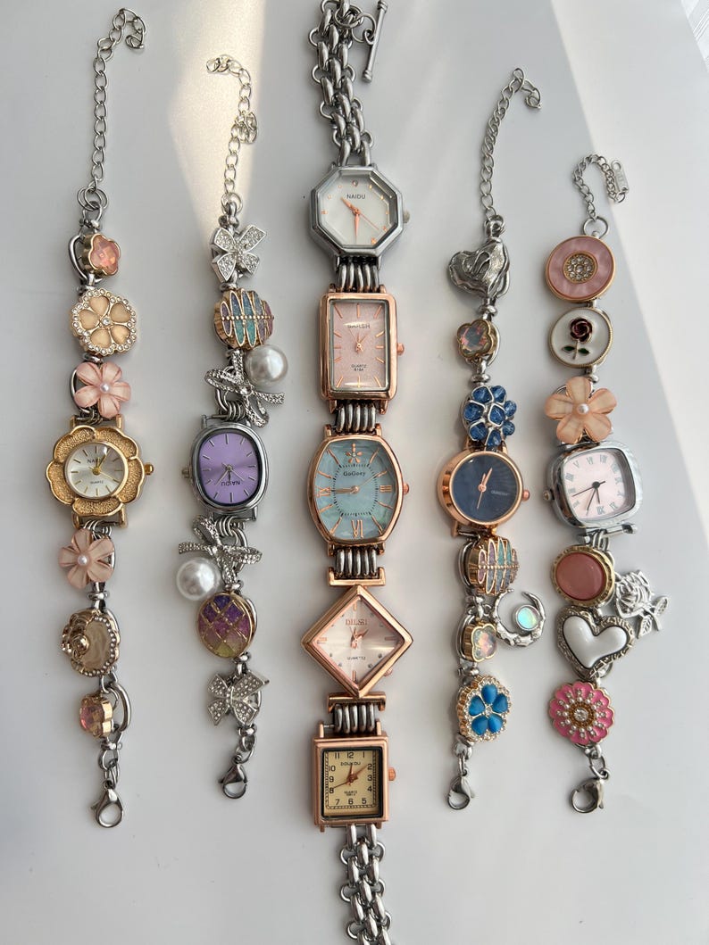 May include: Several decorative bracelet watches with diverse face shapes and embellishments. The watches have silver-tone chains and are decorated with floral, pearl, and gemstone accents. The watch faces come in a variety of colours, including white, pink, and blue.
