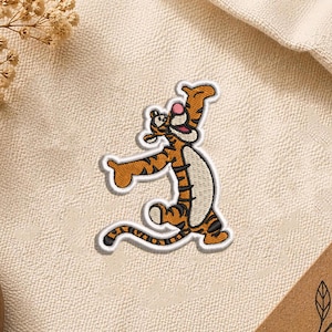 May include: An embroidered patch featuring a cartoon tiger character with orange fur, black stripes, a cream-colored belly, and a pink nose. The character is depicted in a dynamic, jumping pose with arms outstretched and a wide, joyful expression.