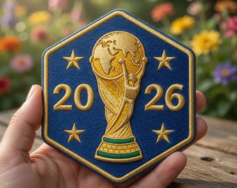 May include: A hexagonal embroidered patch featuring a dark blue background with a gold border. In the centre, a gold trophy design is depicted with the number 20 on the left and 26 on the right. Four gold stars are positioned around the trophy.