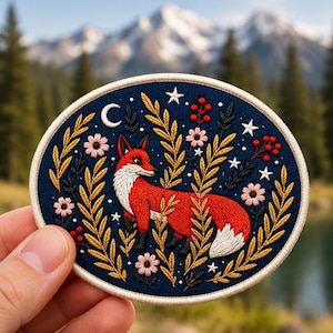 May include: A circular embroidered patch featuring a red fox with a white chest and tail tip, surrounded by golden yellow foliage, small pink flowers, red berries, a white crescent moon, and white stars on a dark navy blue background.