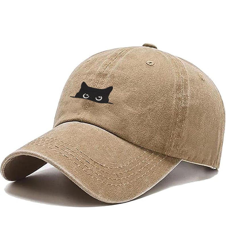 May include: A tan baseball cap with a curved brim. The cap features a black cat graphic peeking over the top. The hat is made of a soft, textured material and has a classic six-panel design.