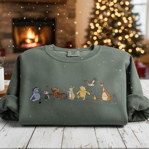 May include: A sage green sweatshirt featuring embroidered cartoon characters. The design includes a blue donkey, a pink pig, a tiger, a rabbit, a bear, a small brown animal, a kangaroo, and a bird. The sweatshirt has a crew neck and long sleeves.