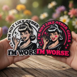 Può includere: Due adesivi circolari con un design retrò di ragazza pin-up. Uno è in bianco e nero, l'altro in nero e rosa. Entrambi presentano il testo "I'M NOT LIKE OTHER GIRLS" e "I'M WORSE".