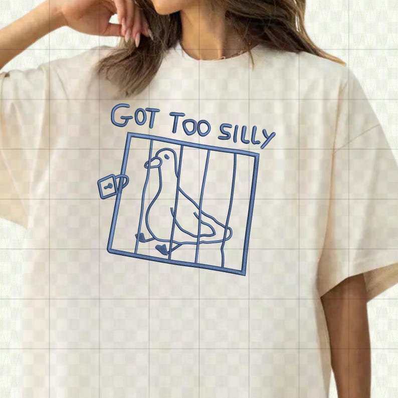 May include: Cream-colored t-shirt with a blue outline drawing of a bird in a cage. The text "GOT TOO SILLY" is above the cage in blue. The shirt has short sleeves and a crew neck.