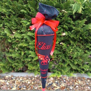 Könnte beinhalten: Ein schwarzer und roter Schultüte mit einer roten Schleife und dem Namen "Elias" bestickt. Die Tüte hat ein rotes Drachenmotiv und den Text "Schulkind 2025".