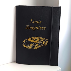 Könnte beinhalten: Schwarzes Notizbuch mit goldgesticktem Text und einem Autodesign. Der Text lautet "Louis Zeugnisse". Ein schwarzes Gummiband sichert das Notizbuch. Das Autodesign ist eine detaillierte Umrisszeichnung eines Sportwagens.