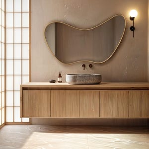 May include: A modern bathroom vanity with a wooden cabinet, a stone sink, and a wavy gold mirror. The vanity is wall-mounted and has a light brown finish. The sink is light grey and has a smooth, rounded shape. The mirror is wavy and has a gold frame.
