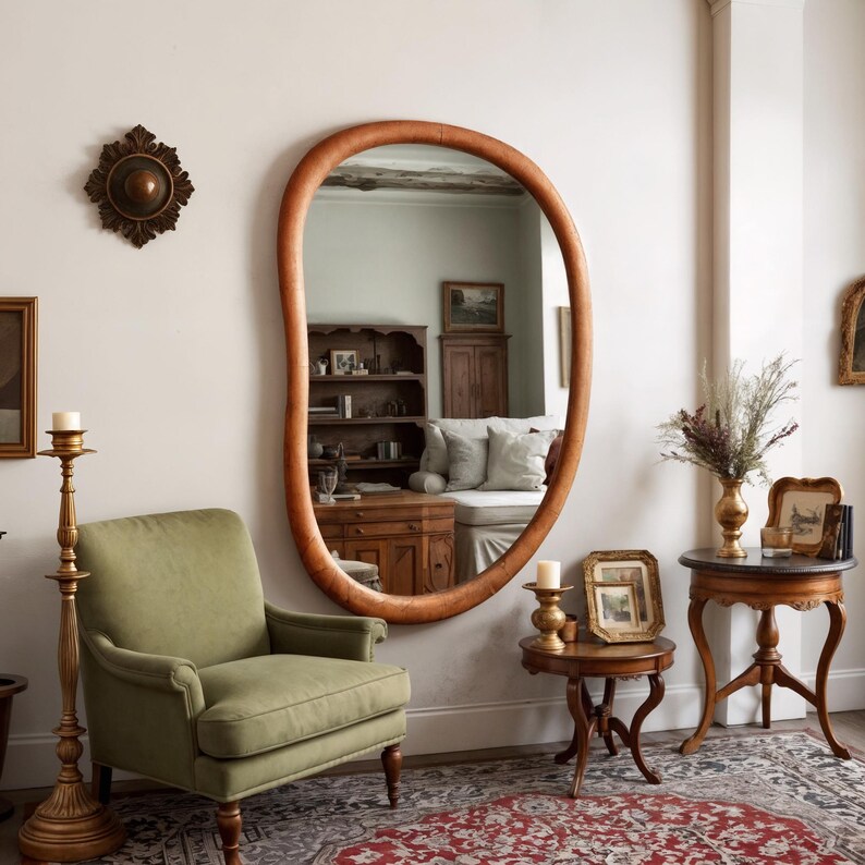 Puede incluir: Un espejo ovalado con marco marr&oacute;n claro cuelga de una pared blanca. Debajo del espejo hay un sill&oacute;n verde. La habitaci&oacute;n tambi&eacute;n cuenta con un candelabro dorado, peque&ntilde;as mesas de madera y una alfombra estampada.