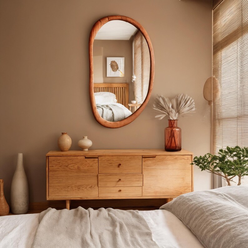 Puede incluir: Un espejo ovalado con marco de madera cuelga de una pared marr&oacute;n sobre un mueble de madera. El mueble tiene tres cajones y dos puertas. Jarrones decorativos y un jarr&oacute;n de cristal con plantas secas est&aacute;n sobre el mueble.