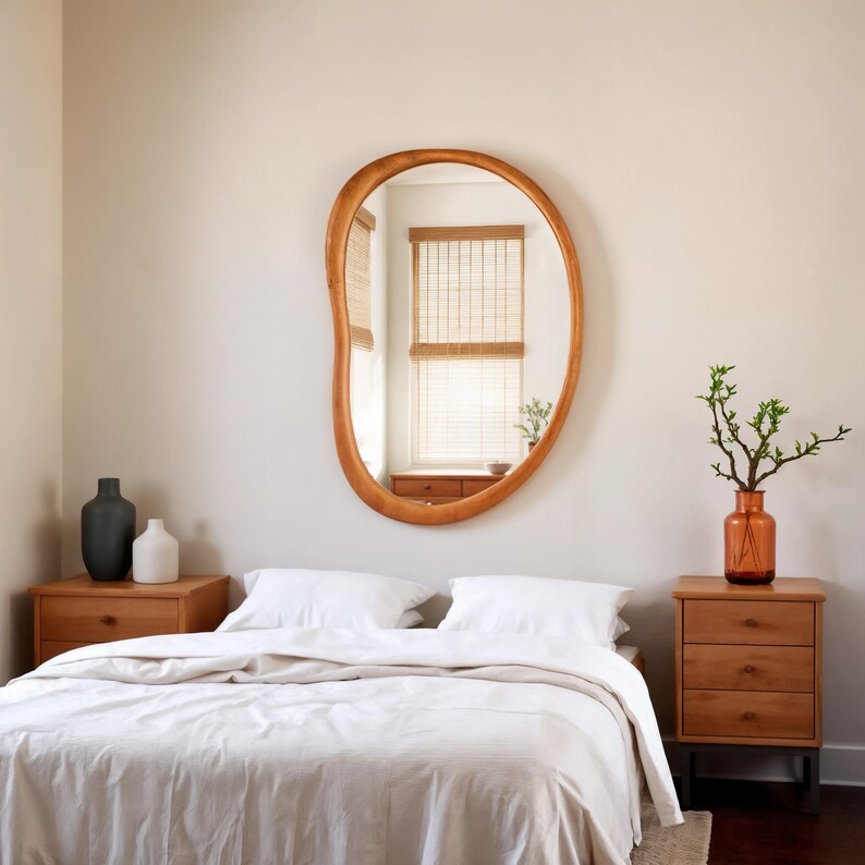Puede incluir: Un dormitorio con un gran espejo de madera de forma org&aacute;nica. El espejo est&aacute; sobre una cama con ropa de cama blanca. Dos mesitas de noche de madera flanquean la cama, una con jarrones y la otra con un jarr&oacute;n de vegetaci&oacute;n. La habitaci&oacute;n tiene una paleta de colores neutros.