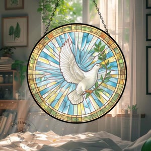 May include: Round stained glass window featuring a white dove with an olive branch, set against a blue and yellow background. The window is framed in black and hangs from a chain. The image is a suncatcher gift.