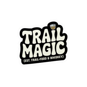 Peut inclure: Un autocollant découpé présentant le texte TRAIL MAGIC en grandes lettres bulles de couleur crème sur un fond noir. Sous le texte, il est écrit (EST. TRAIL-FOOD & WHISKEY) en petites lettres blanches, avec une icône de tasse au-dessus.
