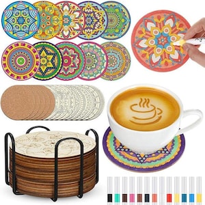 May include: A set of circular wooden coasters featuring intricate mandala patterns, including finished colorful designs and blank versions for customization. The set includes a black metal storage rack, a white ceramic coffee cup, and markers.