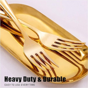 May include: Close-up of gold-colored forks resting on a matching rectangular tray. The forks have a sleek, modern design with four tines. The tray and forks have a shiny, reflective surface. Text at the bottom reads "Heavy Duty & Durable" and "Easy to use every time."