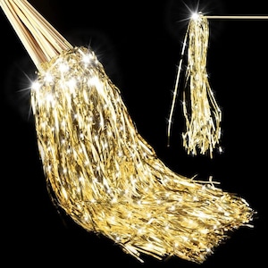 May include: A close-up of a gold metallic fringe decoration with a bundle of wooden sticks at the top. The fringe is long and flowing, with a shiny, reflective surface. The background is black.