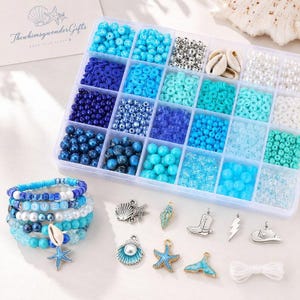 May include: A clear plastic organizer box filled with various blue, white, and turquoise beads, including letter beads, pearls, and shells. Beside the box are several finished beaded bracelets and metal charms shaped like shells, stars, and boots.