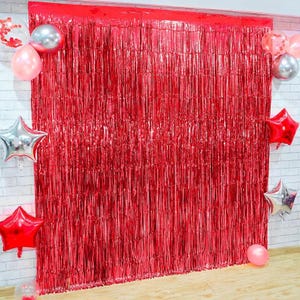 May include: Red foil fringe curtain backdrop for parties and events. The curtain is made of thin strips of red foil that hang down from a horizontal rod. The curtain is a popular backdrop for photo booths and other party decorations.