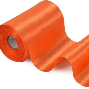 May include: A roll of bright orange satin ribbon. The ribbon is unwound, revealing a smooth, shiny texture. The roll is made of a cardboard core. The ribbon is suitable for crafts, gift wrapping, and decorations.