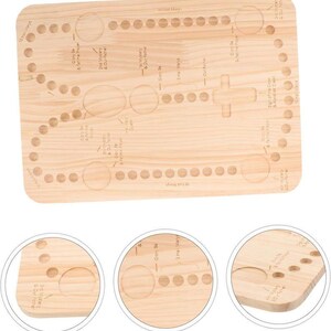 May include: A light-colored wooden rosary board with engraved circles and text. The board features a cross and text that reads "10 Hail Marys", "Our Father", and "Glory Be". The board is rectangular with rounded corners.