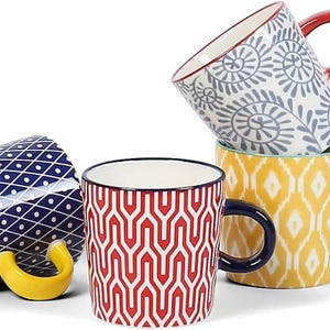May include: A collection of ceramic mugs with various patterns and colors. One mug is navy blue with white polka dots, another is red and white geometric, and others feature floral and geometric designs. Each mug has a different colored handle.