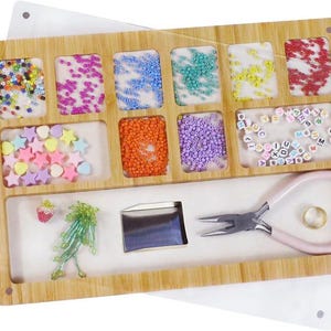 May include: A wooden bead organizer with nine compartments for storing beads, charms, and other jewelry making supplies. The organizer also includes a small tray for tools, a pair of pliers, and a ring.