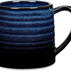 May include: A ceramic mug with a dark blue and black gradient. The mug has a textured, horizontal striped pattern and a large, curved handle. The rim is a lighter blue, and the handle is glossy black.