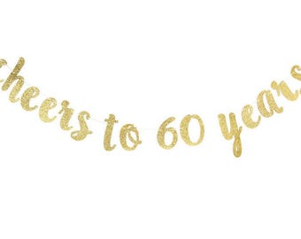 May include: A gold glitter banner that reads "cheers to 60 years" in a cursive font. The banner is strung on a thin white string, perfect for a 60th birthday celebration. The background is plain white.